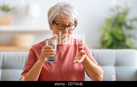 Femme âgée tenant une pilule et un verre d'eau douce, prenant des médicaments contre les maux de tête, les douleurs à l'estomac ou prenant des vitamines, des médicaments de sédation. Banque D'Images