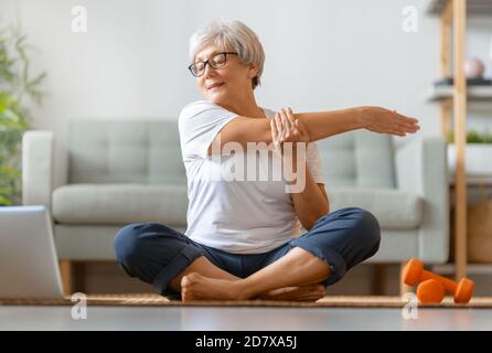 Femme senior en activité regardant des cours en ligne sur ordinateur portable tout en faisant de l'exercice à la maison. Banque D'Images