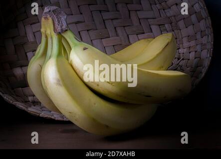 Bananes sur une table rustique en bois avec un panier mexicain fait à la main sur le fond et moody lumière, chiaroscuro technique, ou photo de style baroque Banque D'Images