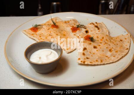 Yantayk avec saumon, caviar rouge, servi avec sauce crème aigre. Repose sur une plaque ronde blanche. Banque D'Images