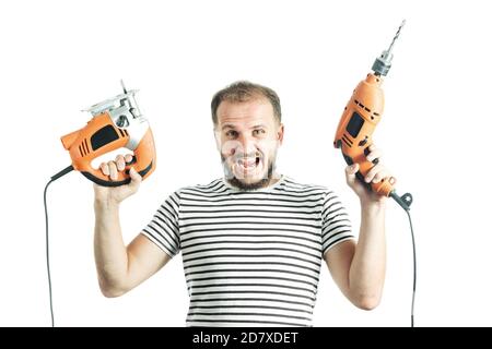 Un homme hurlant dans un T-shirt rayé, tient une perceuse et une scie électrique dans ses mains. Isolé sur fond blanc Banque D'Images