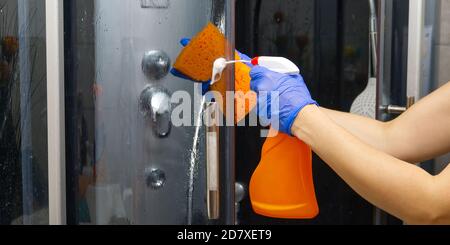 Nettoyage des cabines de vapeur de douche des dépôts de calcium. Nettoyage dans la salle de bains. Mains dans les gants avec un chiffon et détergent lave la douche et le verre Banque D'Images