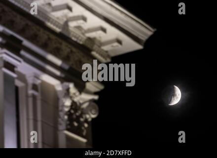 Premier quart de lune sur ciel sombre avec des parties du bâtiment au premier plan Banque D'Images