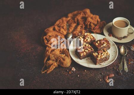 Les morceaux carrés de délicieux gâteau au caramel avec des arachides et noix du brésil servies avec du café au lait Banque D'Images