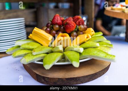 Fruits tropicaux: guava en tranches, fruits jaques, raisins, fraises sur le plat servi sur la table décorée rester à l'extérieur pendant la destination mer Banque D'Images