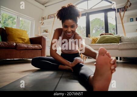 Femme africaine heureuse en bonne santé dans les vêtements de sport faisant l'exercice d'étirement à à la maison sur le tapis de fitness pendant le verrouillage du virus corona Banque D'Images