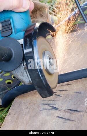 Des étincelles s'échappent du dessous du disque de la scie abrasive circulaire manuelle lors de la découpe du flexible haute pression. Mise au point sélective. Banque D'Images