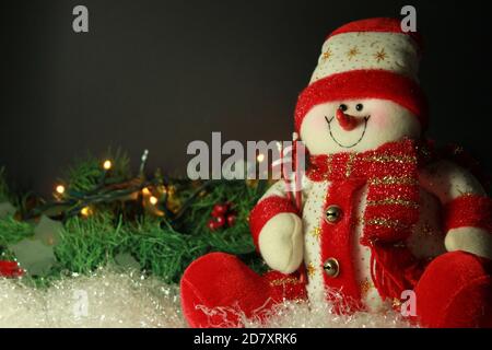 Arrière-plan noir avec un adorable bonhomme de neige au premier plan avec skis et une couronne de pin avec des lumières de Noël, espace d'écriture Banque D'Images