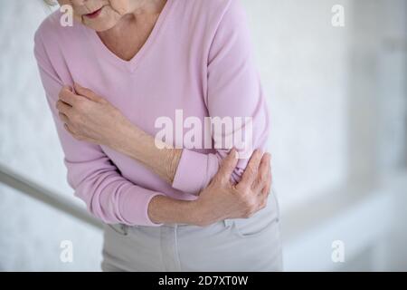 Femme âgée en chemise rose souffrant de douleurs dans le coude Banque D'Images