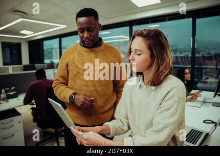 Femme de marque caucasienne analysant la conception de la mise en page d'un collègue de sexe masculin sur une tablette numérique au bureau Banque D'Images