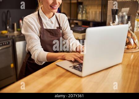 La vendeuse en uniforme dactylographiant le rapport sur l'ordinateur dans le café bar Banque D'Images