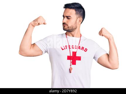 Jeune homme beau portant l'uniforme de maître-nageur montrant les bras muscles souriant fier. Concept de forme physique. Banque D'Images