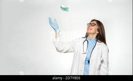 Souriante femme jeune médecin européen jeter le masque après avoir réussi à vaincre le coronavirus. Banque D'Images