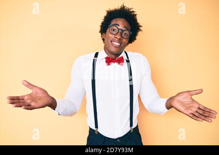 Beau afro-américain homme avec les cheveux afro porter hipster élégant look sans indice et expression confuse avec les bras et les mains soulevées. Doute concept. Banque D'Images
