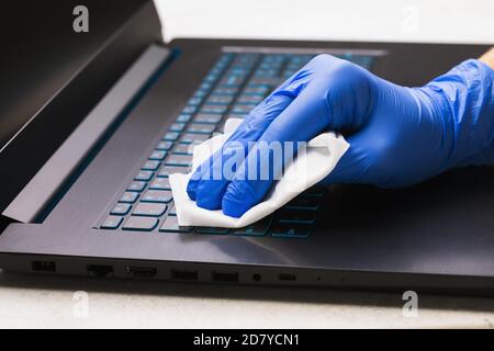 La main de l'homme dans un gant nettoie le clavier de l'ordinateur portable avec un agent antibactérien pour protéger contre l'épidémie de covid-19 maladie. Nettoyage de la surface Banque D'Images