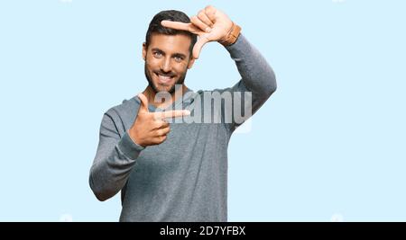 Beau hispanique homme portant des vêtements décontractés souriant faisant cadre avec les mains et les doigts avec le visage heureux. Créativité et concept de photographie. Banque D'Images