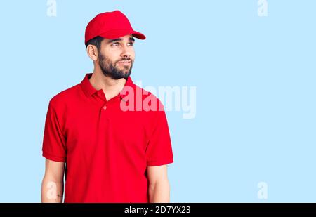 Jeune homme beau avec une barbe portant un uniforme de livraison souriant regardant sur le côté et regardant loin de penser. Banque D'Images