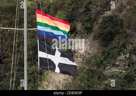 Un drapeau arc-en-ciel et un drapeau Cornouair St Piran volant du mât d'un bateau amarré sur le Gannel à Newquay en Cornouailles. Banque D'Images