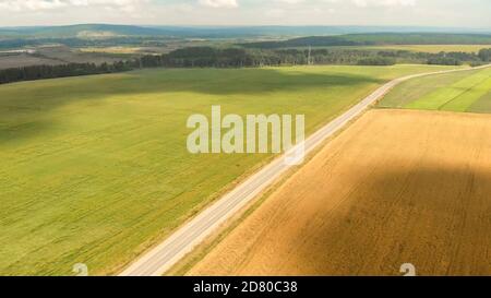 Large champ vert avec ombres nuages flottantes entre les forêts et la route asphaltée avec des voitures de conduite contre une silhouette de paysage vallonnée. Banque D'Images