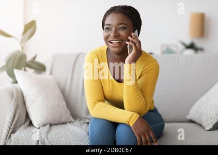 Appel téléphonique. Joyeuse jeune femme afro-américaine parlant au téléphone portable à la maison Banque D'Images