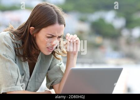 Femme stressée forçant la vue portant des lunettes de vue lisant ordinateur portable à l'extérieur Banque D'Images