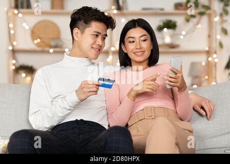 Couple Shopping avec smartphone et carte de crédit dans le salon Banque D'Images