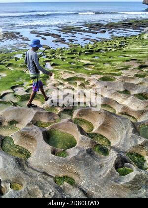 Pêcheur balinais local marchant le long de rochers érodés et de mousse verte à Balangan Beach, Bali, Indonésie Banque D'Images