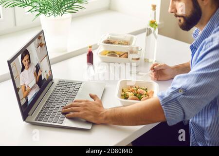 Jeune homme ayant un déjeuner virtuel avec sa femme ou sa petite amie pendant pause au travail ou au bureau à domicile Banque D'Images