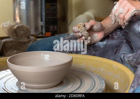 femme créant de la poterie à une roue de potiers, les mains couvertes d'argile. Banque D'Images