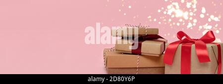 Bannière avec pile de boîtes-cadeaux sur fond rose. Composition des fêtes avec bokeh doré brillant. Banque D'Images