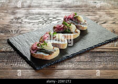 Sandwichs ouverts avec poisson, fromage à la crème, oignon mariné, microverts et caviar sur tableau d'ardoise noire Banque D'Images