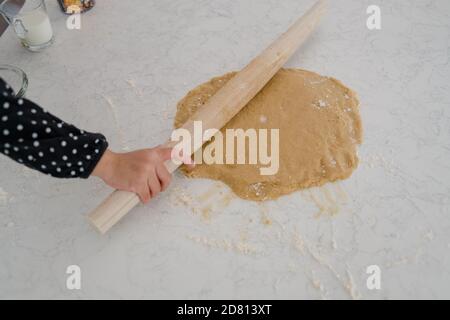 Petite fille utilisant une broche roulante pour rouler la pâte à biscuits Banque D'Images