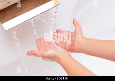 L'enfant lave ses mains avec du savon sous un robinet d'eau propre. Les mains d'un enfant savonneux se rapprochent sur un fond blanc. Concept d'hygiène. Maladie preventi Banque D'Images