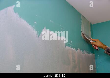 Un constructeur professionnel lisse le mur avec du mastic à la spatule placé sur une surface plane de réparation de mur dans son propre appartement. Banque D'Images