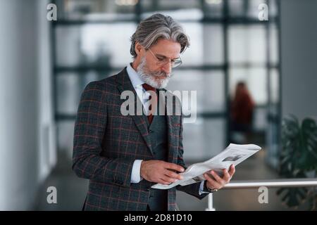 Homme d'affaires senior en costume et cravate avec cheveux gris et la barbe tient le journal entre les mains Banque D'Images