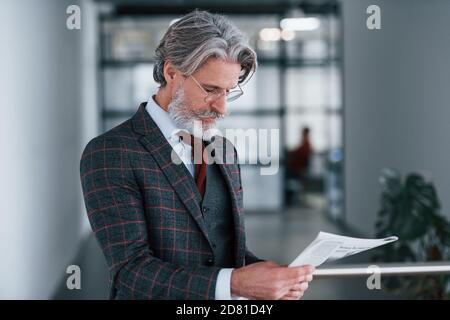 Homme d'affaires senior en costume et cravate avec cheveux gris et la barbe tient le journal entre les mains Banque D'Images