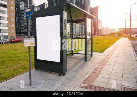 Arrêt de bus vide avec un abri le long d'une rue au coucher du soleil. Un panneau d'affichage vierge se trouve sur l'un des côtés de l'abri. Copier l'espace. Banque D'Images