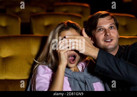 Un couple regardant un film thriller dans le cinéma, les hommes utilisent leurs mains pour fermer les yeux de sa petite amie. Banque D'Images