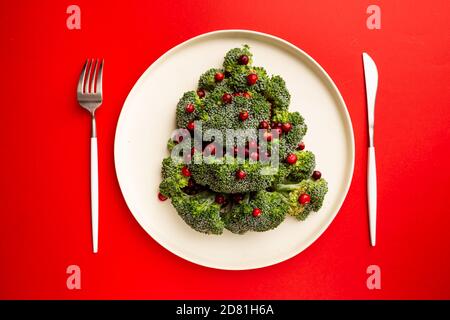 Arbre de Noël fait de brocoli et de canneberge sur plaque blanche et fond rouge, vue de dessus Banque D'Images