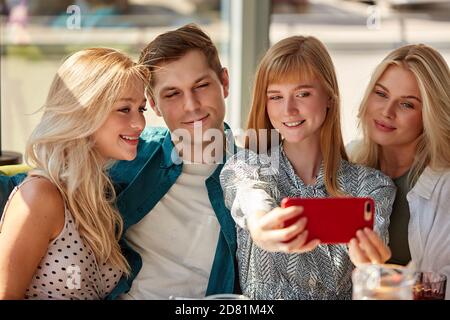 portrait de belles femmes prenant des photos sur un téléphone portable, quatre jeunes en vêtements décontractés sourient à l'appareil photo du smartphone, posant. dans une pièce lumineuse Banque D'Images