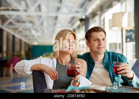 un couple charmant et élégant s'assoit en discutant avec des amis devant eux dans le restaurant, tient des verres de jus de fruit doux entre les mains, passe du temps ensemble, fête Banque D'Images