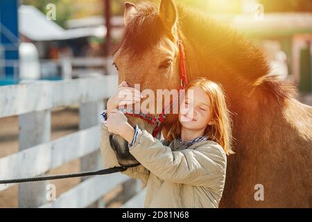 Bonne fillette au gingembre tenant le museau du cheval, touchant la tête du cheval avec ses Banque D'Images