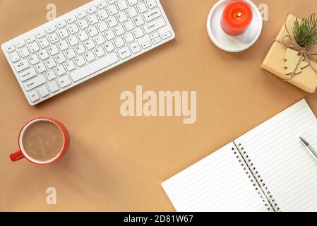 Espace de travail confortable avec clavier, bloc-notes, cadeau dans une boîte, bougie, tasse de café ou cacao sur fond beige. Concept de nouvel an ou de Noël. Haut Banque D'Images