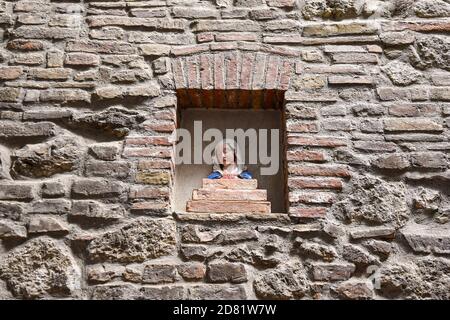 Gros plan d'un vieux mur en brique et pierre avec un buste en céramique peint de Sainte Marie à l'intérieur d'une niche dans la vieille ville de San Gimignano, Sienne, Toscane, Italie Banque D'Images