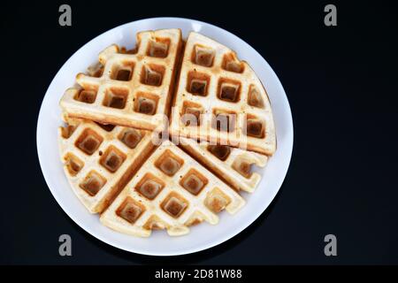 Gaufres belges dans une assiette blanche sur une table en verre noir. Petit déjeuner sain, morceaux de cachets classiques fraîchement préparés Banque D'Images