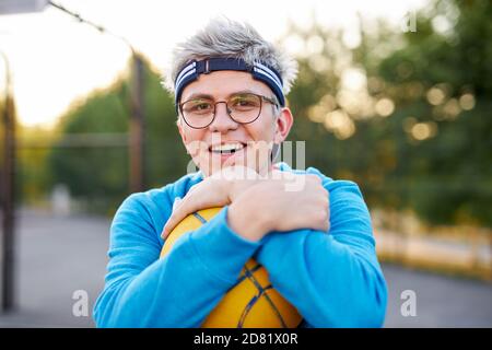 jeune garçon de race blanche jouant au basket-ball, un homme beau dans des vêtements de sport décontractés seul au terrain de jeu de basket-ball, pratique Banque D'Images