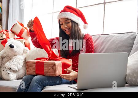 Excitée fille indienne porter chapeau de père noël ouvre cadeau vidéo d'appel de famille sur Noël. Banque D'Images