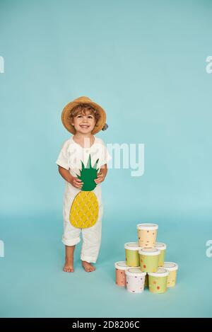 Petit garçon en chapeau de paille posant dans le studio de photo sur fond bleu. Banque D'Images