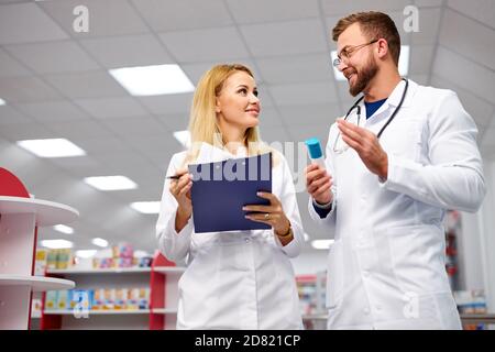 une équipe de jeunes chimistes ou buveurs caucasiens discutant des médicaments, vérifier les indications médicales, dans les robes médicales blanches, sur le lieu de travail Banque D'Images