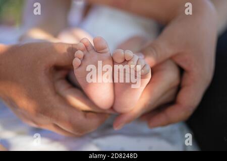 Les pieds de la petite fille dans les mains des parents. Faisceau de soleil. Extérieur. Gros plan Banque D'Images